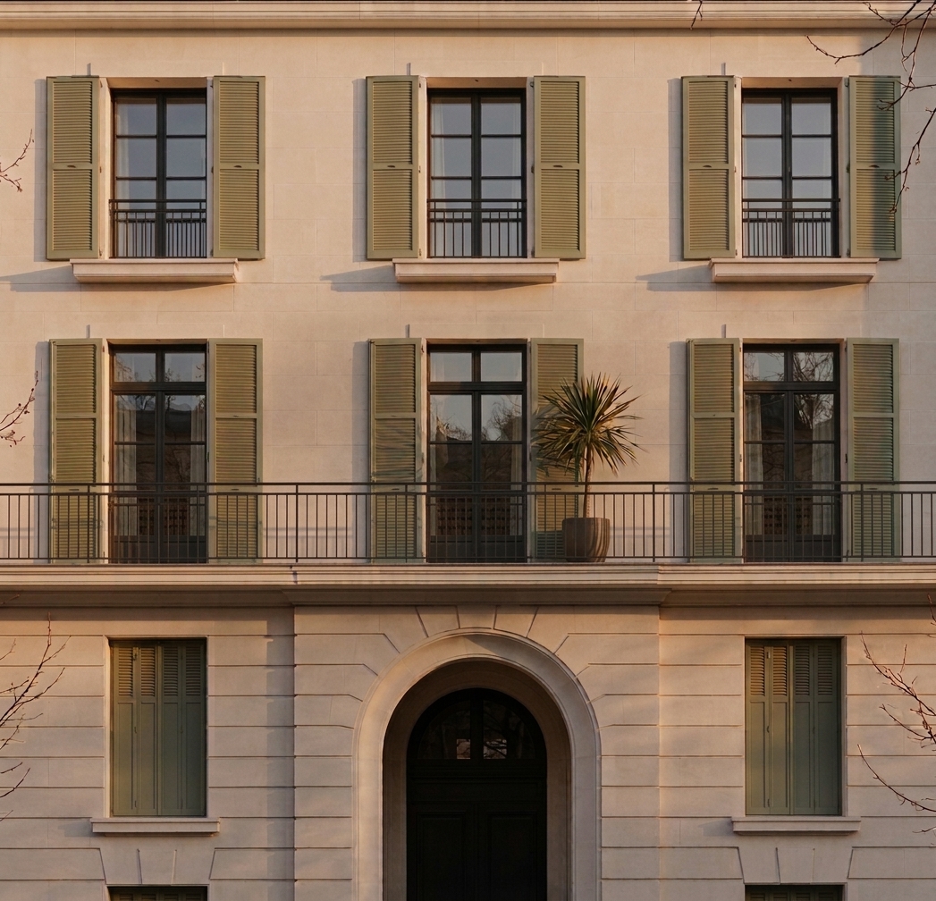 Façade française ravalée en pierre claire avec volets persiennés et balcon filant